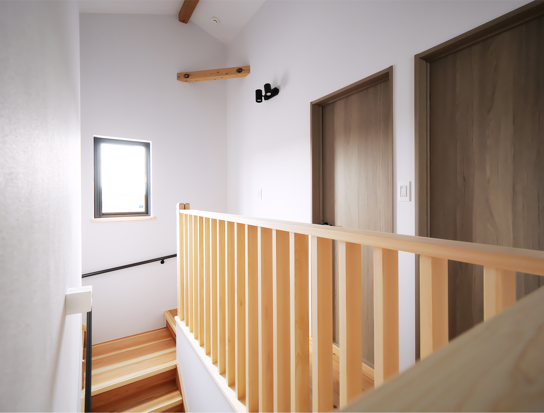 階段横に設けた木製手すりと白壁の2階通路